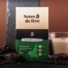 Une tablette de chocolat dans un emballage vert. Autour, un verre de Latte macchiatto, du poivre, et des dattes.